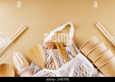 Wooden cutlery and string bag on beige background. Disposable paper cups and glassware on earth color background. Zero waste concept. Copy space. Top Stock Photo