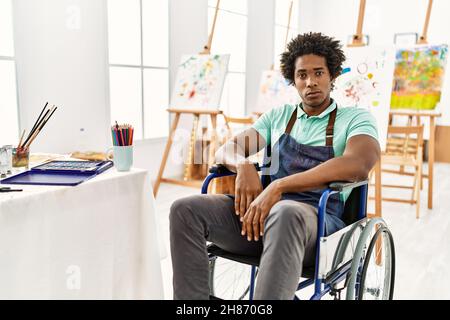 Young african american artist man sitting on wheelchair at art studio relaxed with serious expression on face. simple and natural looking at the camer Stock Photo