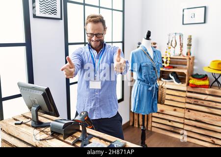 Middle age man working as manager at retail boutique pointing fingers to camera with happy and funny face. good energy and vibes. Stock Photo