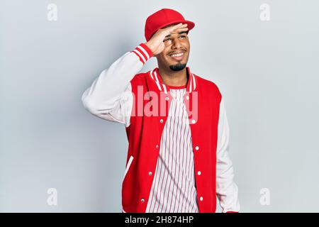 Young african american man wearing baseball uniform very happy and smiling looking far away with hand over head. searching concept. Stock Photo