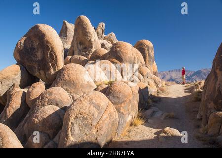 Alabama Hills National Scenic Area, Lone Pine, California, USA. Visitor looking up in awe at typical outcrop of smooth granite boulders. Stock Photo