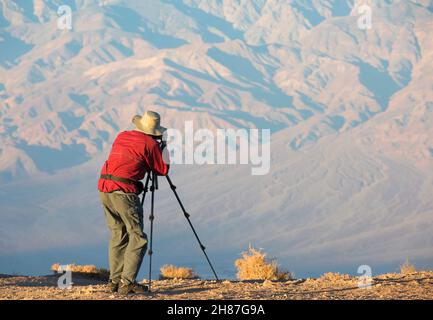 Death Valley National Park, California, USA. Photographer at Dante's View shooting the distant Panamint Range with tripod from cliff edge, sunrise. Stock Photo