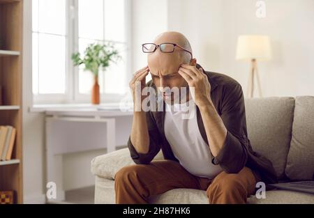 Confused man sitting on couch and thinking trying to understand or remember something Stock Photo