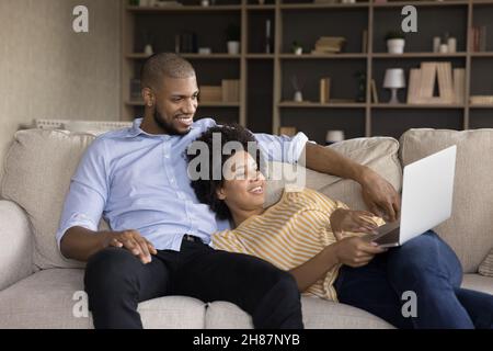 Happy relaxed Black married couple resting on sofa Stock Photo