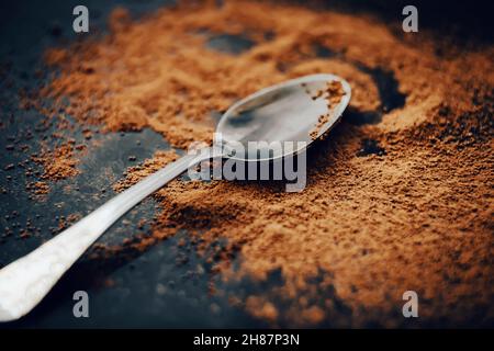 A beautiful silver teaspoon with patterns lies on the scattered fragrant cocoa powder. A delicious drink in the morning. Hot chocolate. Stock Photo