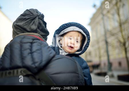 Cute little baby boy in his fathers arms. Dad and son having fun on chilly winter day in city park. Adorable son being held by his daddy. Stock Photo