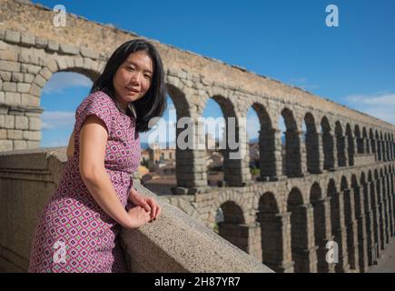 Attractive Asian girl during vacation in Spain - young happy and beautiful Japanese woman visiting world heritage aqueduct in Segovia enjoying holiday Stock Photo