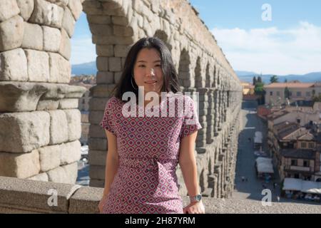 Attractive Asian girl during vacation in Spain - young happy and beautiful Korean woman visiting world heritage aqueduct in Segovia enjoying holidays Stock Photo