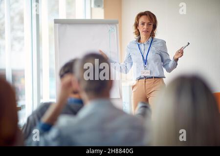 An elderly female businesswoman is giving a lecture to a group of young business people in a working atmosphere in the conference room. Business, peop Stock Photo