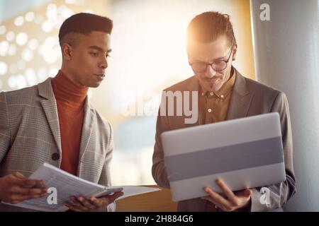Two young businessmen are standing in the hallway and doing some work together in a pleasant atmosphere. Business, people, company Stock Photo