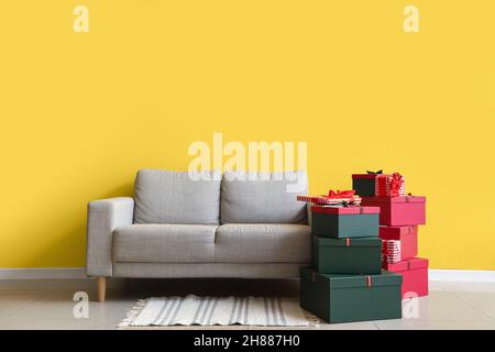 Stack of different Christmas gift boxes on floor near sofa in room Stock Photo