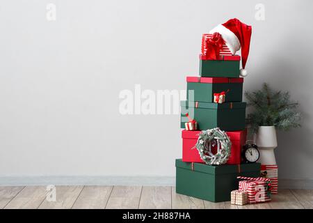 Stack of Christmas gift boxes, alarm clock and vase with fir tree branches on floor near white wall Stock Photo