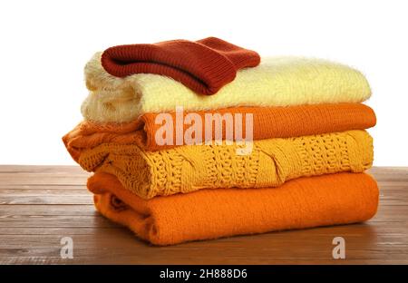 Stack of different stylish sweaters and hat on wooden table against white background Stock Photo
