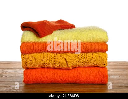 Stack of different stylish sweaters and hat on wooden table against white background Stock Photo