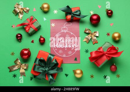 Greeting card with text HAPPY HOLIDAYS, gift boxes and Christmas decor on green background Stock Photo