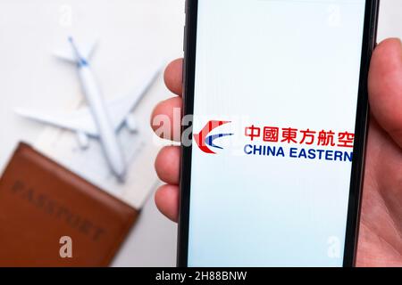 China Eastern Airlines app logo on the screen of mobile phone. A blurry image of a plane, a passport and boarding pass on the background. November 2021, San Francisco, USA Stock Photo
