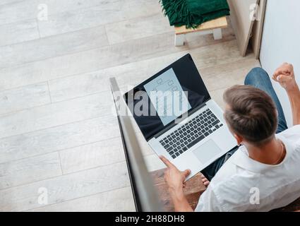young man with a laptop sitting on the steps in his apartment. Stock Photo