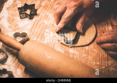 Making gingerbread cookie, cutting heart shape from dough by cookie cutter. Senior  woman making traditional gingerbread biscuit. Close-up old hand Stock Photo