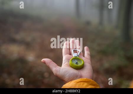 Lost traveler holding compass in her hand. Make decision which way to go from misty forest. Woman hiking in nature Stock Photo