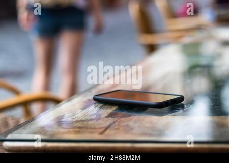 Woman leaving from street restaurant where she forget her mobile phone. Lost smart phone on table at outdoor cafe. Selective focus Stock Photo