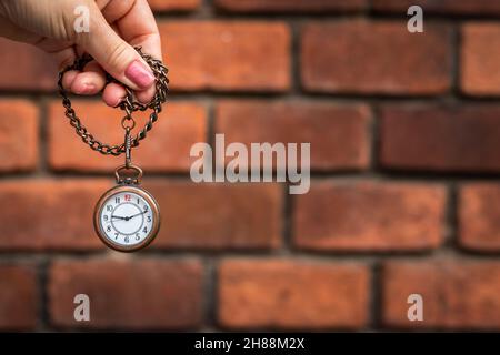 Female hand holding pocket watch against red brick wall. Retro luxury watch with copy space Stock Photo
