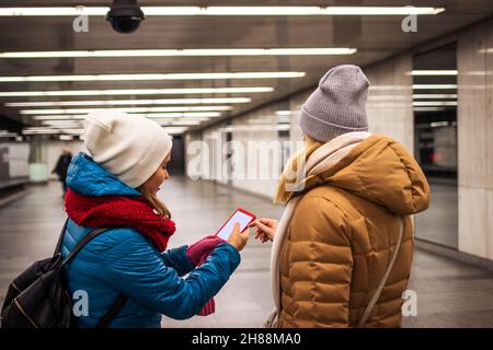 Two women buying ticket to subway by using mobile app. Young tourists using smart phone in subway station. Traveling in city Stock Photo