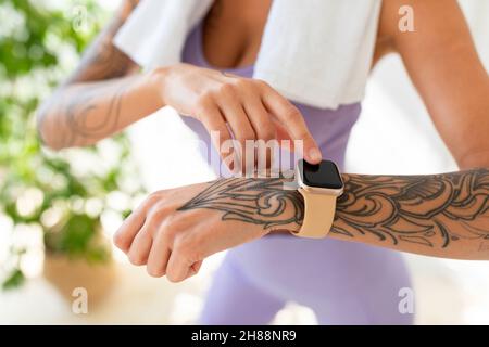 Young tattooed woman looking at activity fitness tracker during workout break, checking heart rate and burned calories Stock Photo