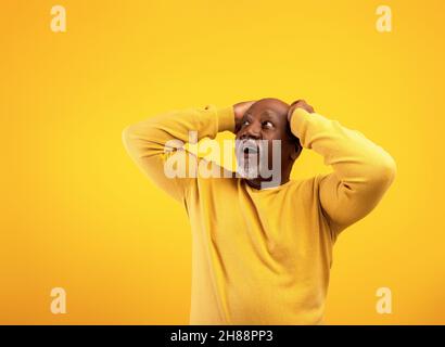 Amazed emotional senior black man holding his head in shock, looking at copy space for your text or advertisement Stock Photo