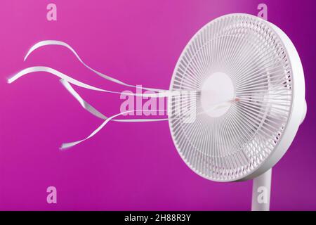 The electric fan is white with pink ribbons fluttering in the wind on a pink background. Free space, minimalistic style. Stock Photo