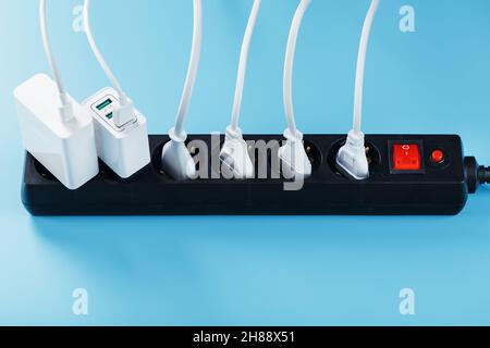 Surge protector with connected white wires of electrical appliances on a blue background. Free space Stock Photo