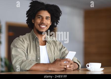 Portrait Of Young Black Guy Relaxing With Smartphone At Table In Cafe Stock Photo