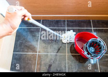Adult asian male mopping tiled floor with a rope mop and a mop bucket Stock Photo