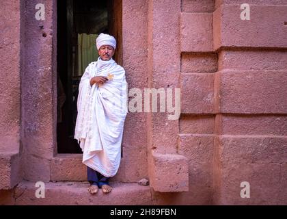 Lalibela, Ethiopia - May 23, 2021: One priest outside a church, holding a golden cross and wearing white clothing and a turban Stock Photo