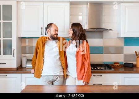 Happy young couple talking at home in kitchen. Family Husband and wife enjoying spending time together while standing in apartment interior. Love in Stock Photo