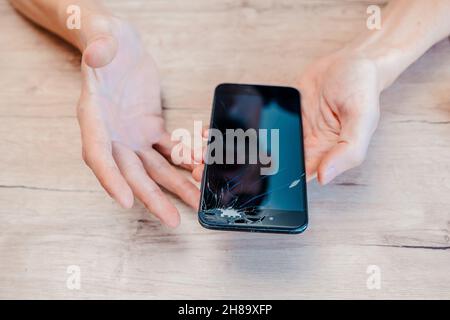 smartphone with a cracked screen in the hands of a young man. Stock Photo