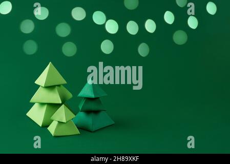 Three green paper Christmas trees on green background with bokeh lights paper crafts, Christmas concept, copy space. Stock Photo