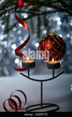 Christmas decorations. Two burning candles in a candlestick, a red ball and streamer ribbon on the Christmas tree. Selective focus Stock Photo