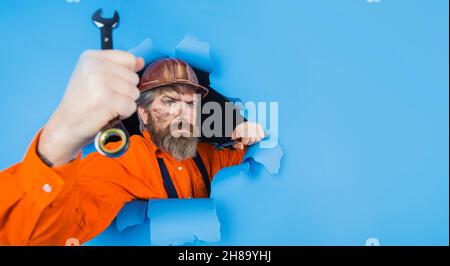 Builder in hardhat with wrench looking through paper hole. Bearded man with spanner. Selective focus. Copy space for Advertising. Stock Photo