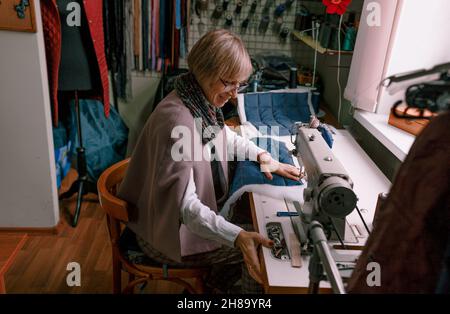 A female dressmaker uses a sewing machine to create custom-made clothes in a workshop. A female seamstress is busy sewing clothes in the workplace. Stock Photo
