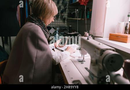 A female seamstress using a mobile phone while working in an atelier. Stock Photo