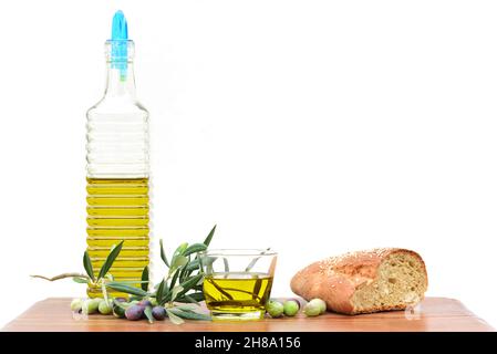 A bottle with olive oil, several branches from the olive tree and olives stand on a table in front of a light background with space for text. On the t Stock Photo