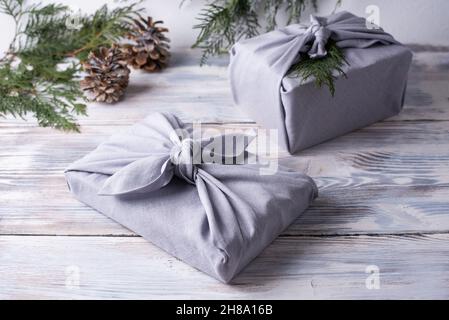 Two christmas gifts wrapped in gray linen cloth on white wooden background, eco-friendly packaging, zero waste concept, furoshiki. Stock Photo