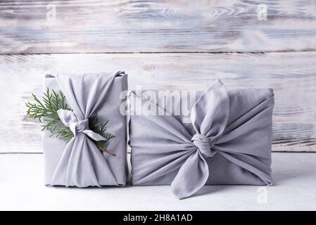 Eco-friendly packaging, zero waste concept, two Christmas gifts wrapped in gray linen cloth on white wooden background, furoshiki. Stock Photo