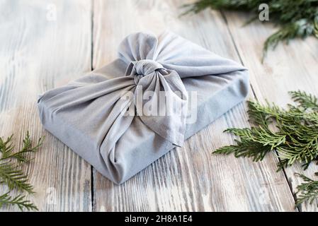 A gift wrapped in cloth on a white wooden background with fir branches, Christmas zero waste and eco-friendly concept. Stock Photo