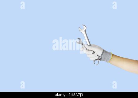 Gloved hands holding wrench, spanner construction tools. Work tools on blue background Stock Photo