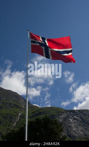 Norwegian national flag in the breeze against a blue sky with mountain ...