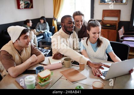 Group of college students sitting at the table and studying together using laptop Stock Photo