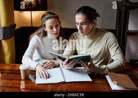College student in eyeglasses reading a book and studying together with the teacher at the table Stock Photo