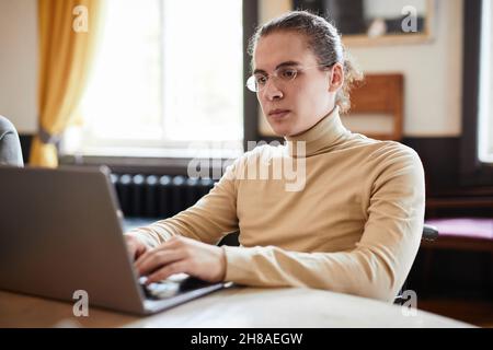 College student in eyeglasses concentrating on his online work on laptop at the table Stock Photo