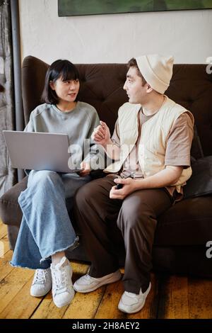 Two students sitting on sofa using laptop and discussing online education together in the room Stock Photo